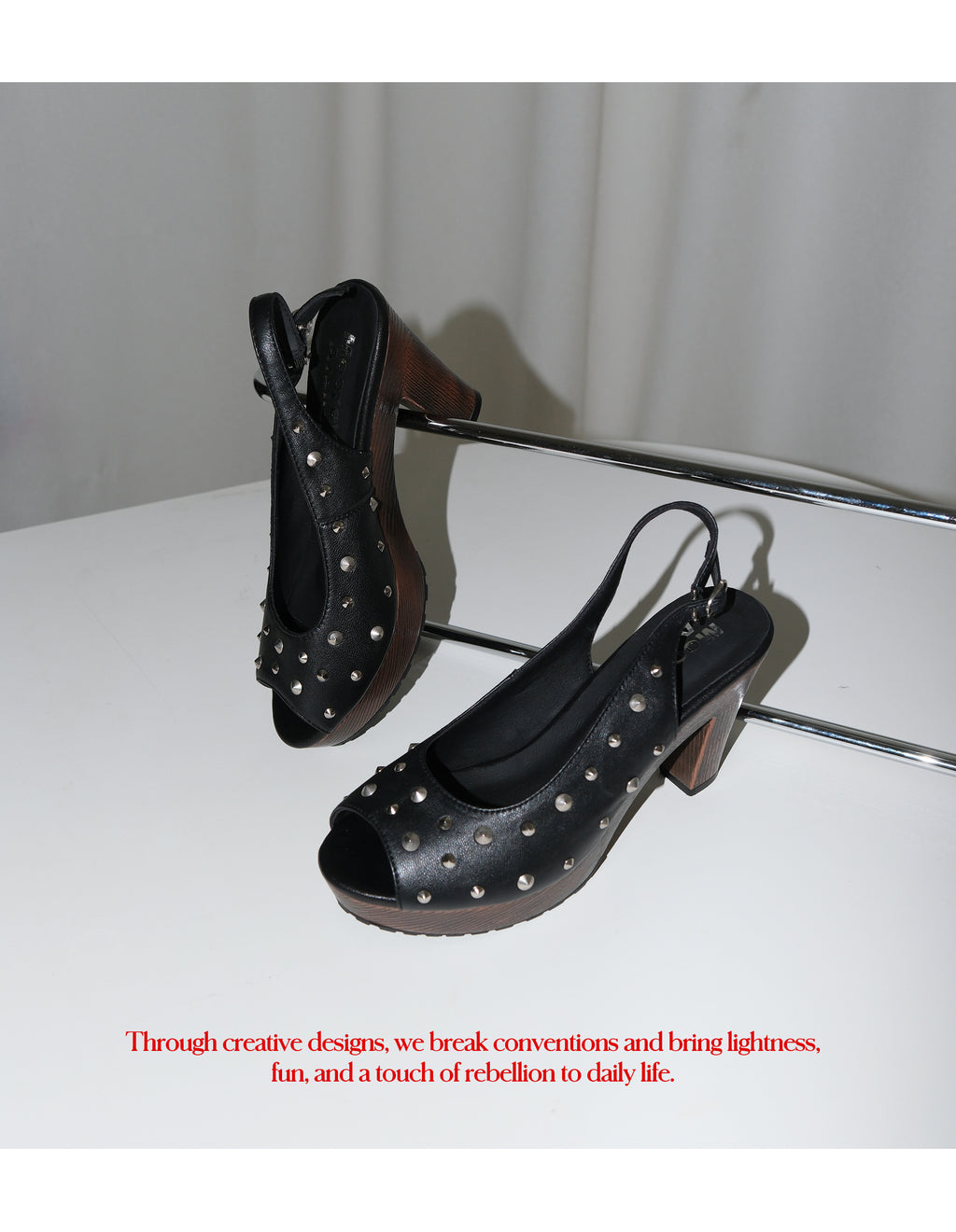 Two black studded leather slingback peep toe heels placed on silver metal rack, side view showing faux wood grain thick block heel and platform sole