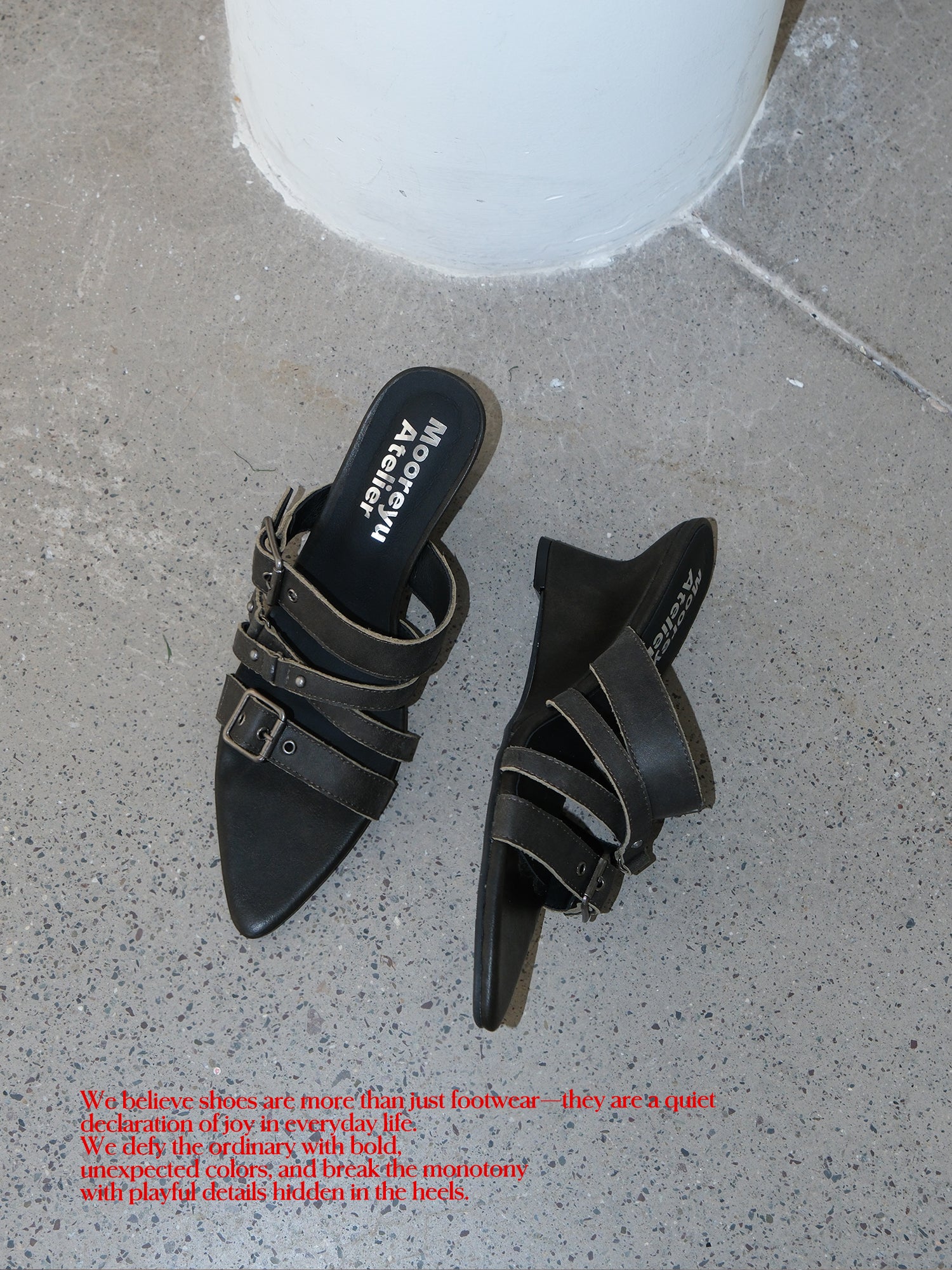 Top-down studio shot of two distressed grey leather buckle wedge mule slides placed on concrete floor