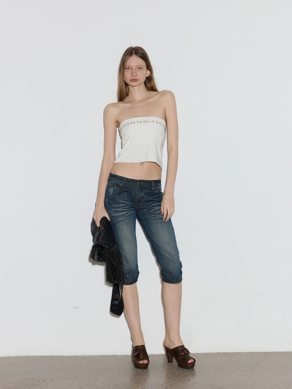 Full-length model shot in white tube top & cropped jeans, holding black fringe bag, wearing vintage brown leather platform mule clogs