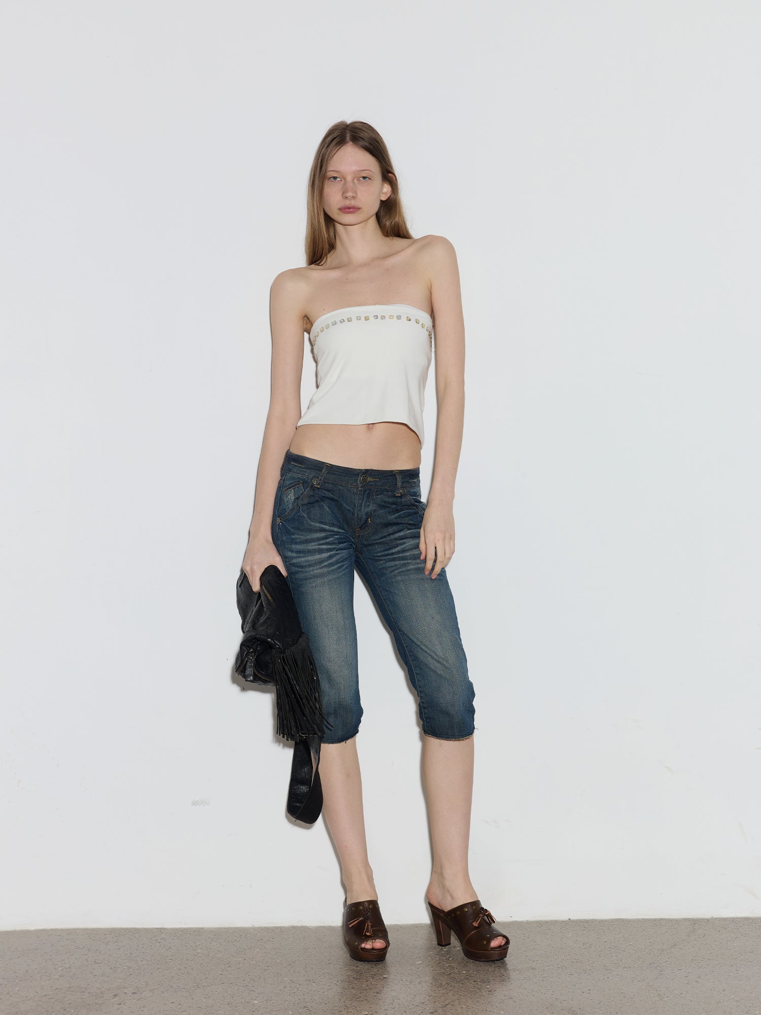 Full-length model shot in white tube top & cropped jeans, holding black fringe bag, wearing vintage brown leather platform mule clogs