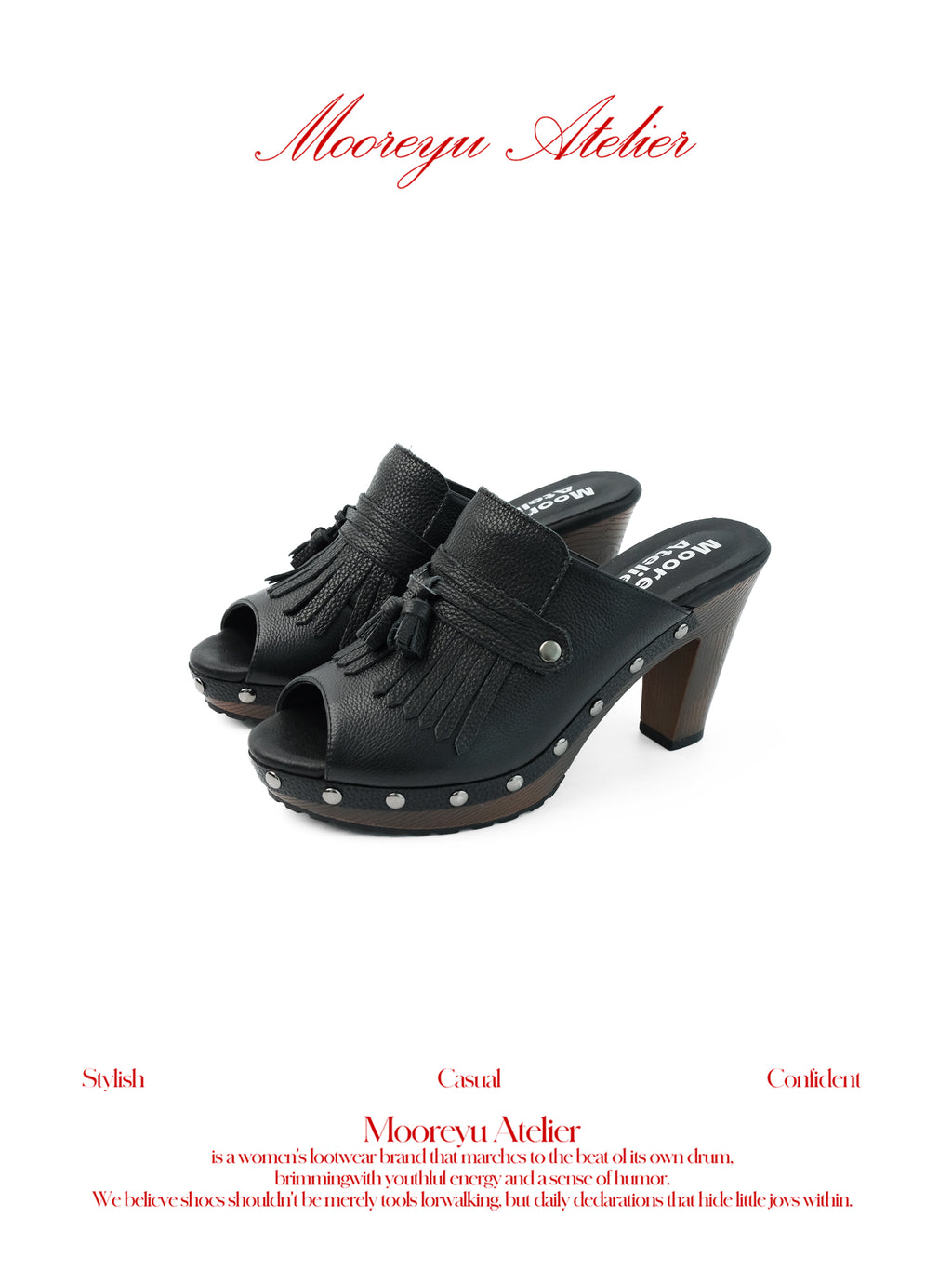White background MOOREYU ATELIER solid black pebbled full grain leather mule clogs, peep toe leather fringe tassels & surrounding silver studs, 10cm faux wood grain platform block heels studio shot