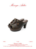 White background studio shot of MOOREYU ATELIER vintage distressed brown leather mule clogs, peep toe brass studs & leather tassels, 10cm faux wood grain platform block heels