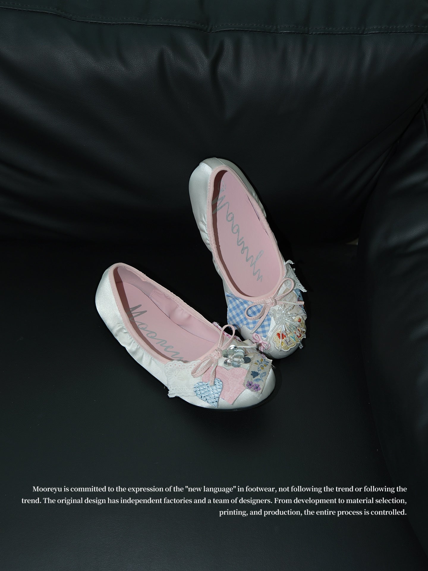 Two pink satin ballet flats with heart embroidery and plaid patch decor placed on black leather sofa, vintage coquette shoe studio shot